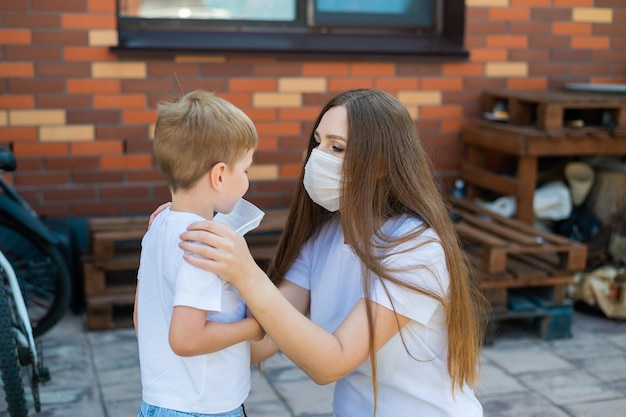 Uma mãe carinhosa coloca uma máscara em seu filho para prevenir a infecção por coronavírus Conformidade com a distância social e as normas sanitárias Mulher e criança ao ar livre