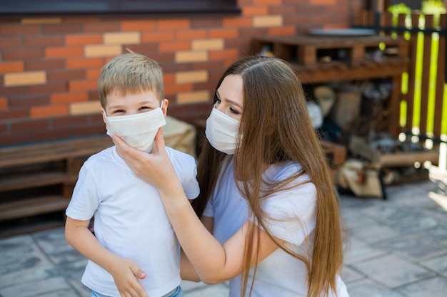 Uma mãe carinhosa coloca uma máscara em seu filho para prevenir a infecção por coronavírus Conformidade com a distância social e as normas sanitárias Mulher e criança ao ar livre