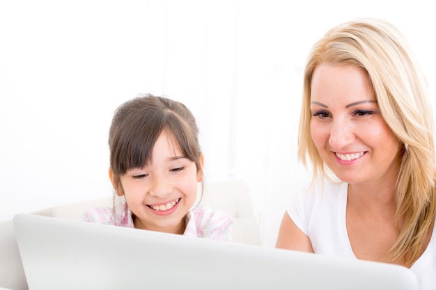 Uma mãe com sua filha olhando para um laptop em casa.