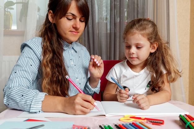 Uma mãe com um filho senta-se à mesa e faz o dever de casa. A criança aprende em casa. Educação escolar em casa.