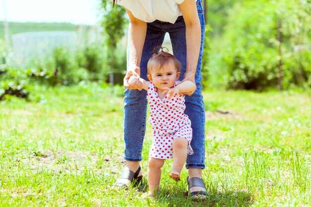 Uma mãe conduz a filha com as mãos na grama do jardim. primeiros passos