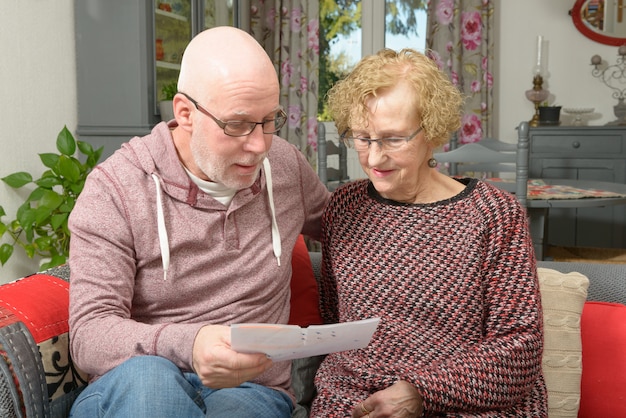 Uma mãe e seu filho adulto olhando papel em um sofá