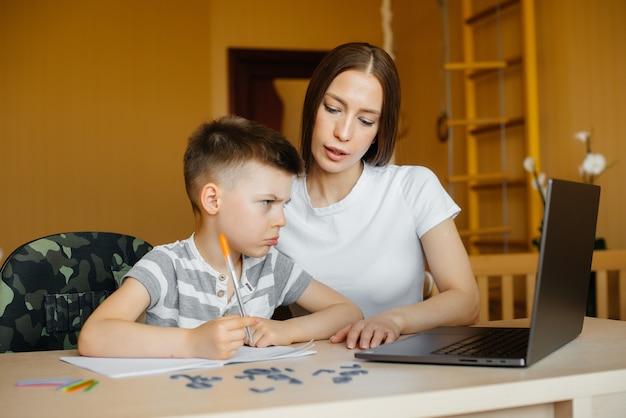 Uma mãe e seu filho estão envolvidos em ensino à distância em casa, na frente do computador. fica em casa, treinando.