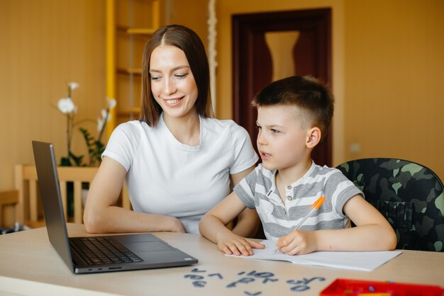 Uma mãe e seu filho estão envolvidos em ensino à distância em casa, na frente do computador. Fica em casa, treinando.