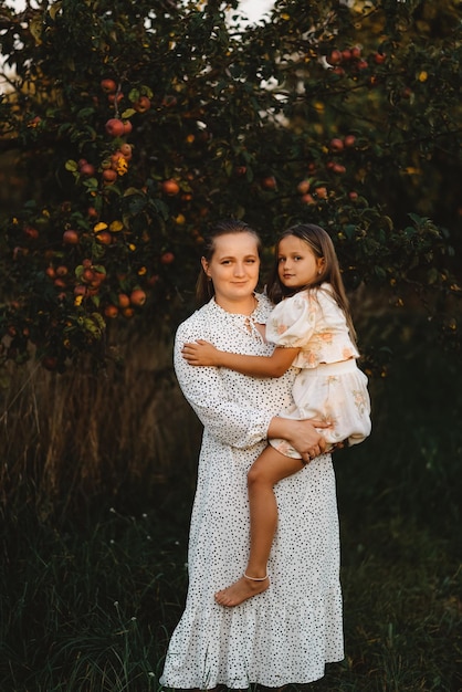 Uma mãe está segurando sua filha em seus braços no jardim perto de uma macieira