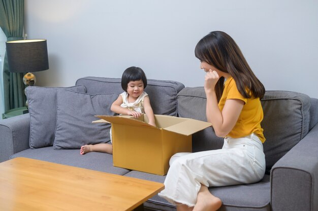 Uma mãe feliz com a filha abrindo uma caixa de papelão na sala de estar de casa