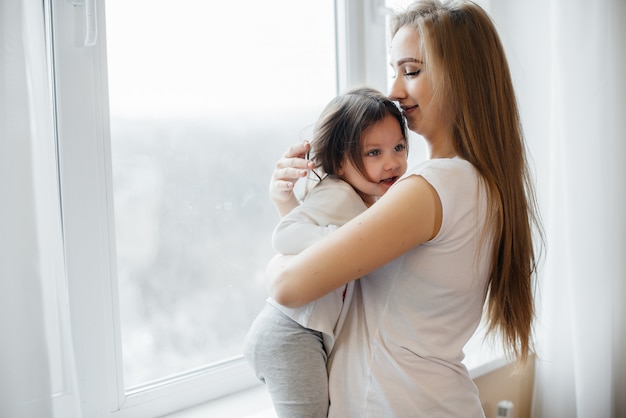 Uma mãe grávida está de pé perto da janela com sua filha.