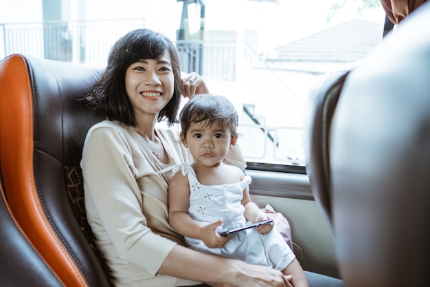 Uma mãe sorridente e feliz e uma garotinha segurando um celular enquanto estão sentadas perto da janela no ônibus