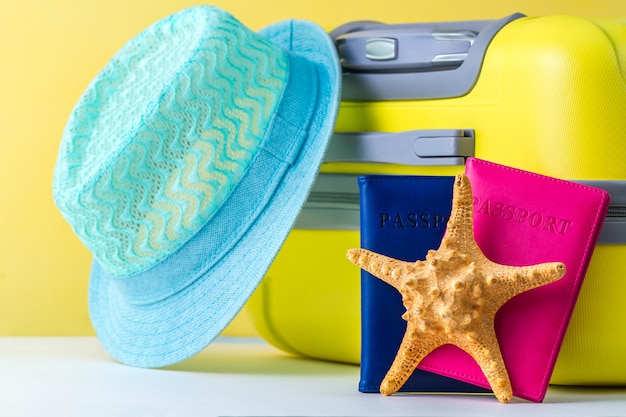 Uma mala de viagem amarela brilhante, passaportes, chapéu azul e conchas. Conceito de viagens. Lazer, férias