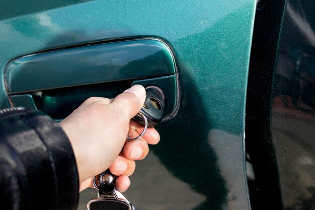Uma mão abre a porta de um carro verde com uma chave