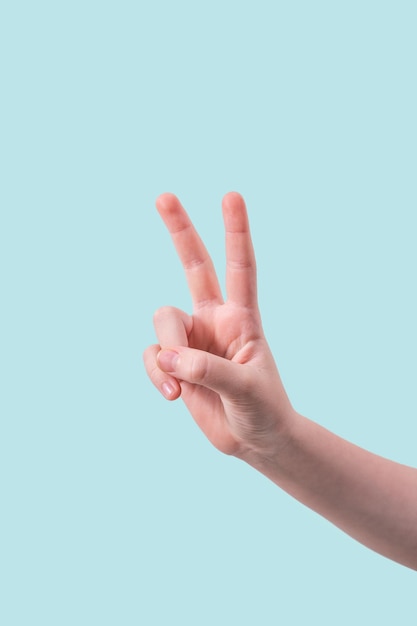 Uma mão adolescente ou feminina faz um gesto de boas-vindas com dois dedos em um fundo azul O conceito de um sinal de paz e bondade das mãos Banner para simulação ou publicidade Espaço livre para texto