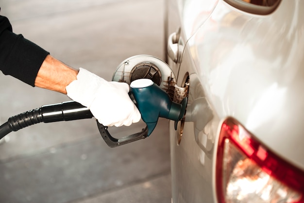 Uma mão adulta reabastecer o tanque de gasolina do carro com um bico em um posto de gasolina