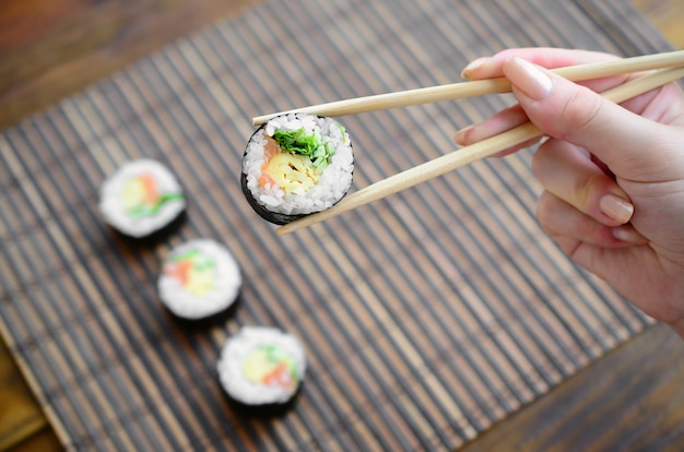 Uma mão com pauzinhos detém um rolo de sushi em uma palha de bambu