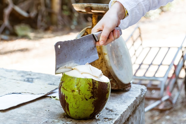 Uma mão com um cutelo que corta coco verde fresco.