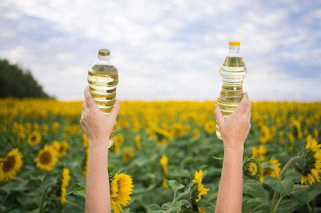 Uma mão com uma garrafa de óleo de girassol dourado levantada contra o fundo de um campo de girassóis florescendo em um espaço de cópia ensolarado