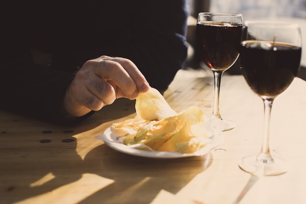 Uma mão de homem com uma batata de batatas fritas e dois copos de vermute. Aperitivo espanhol