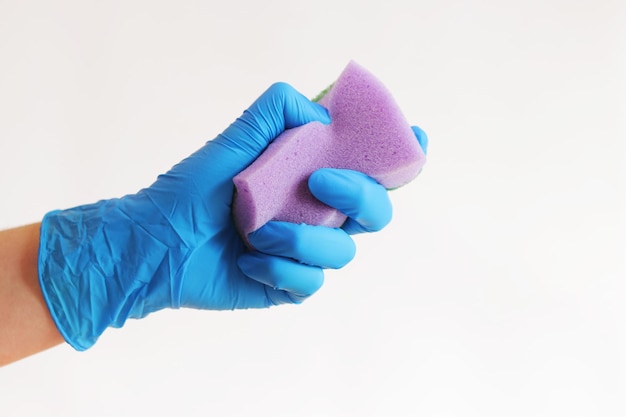Uma mão de mulher em uma luva azul de látex com uma esponja roxa limpando pratos