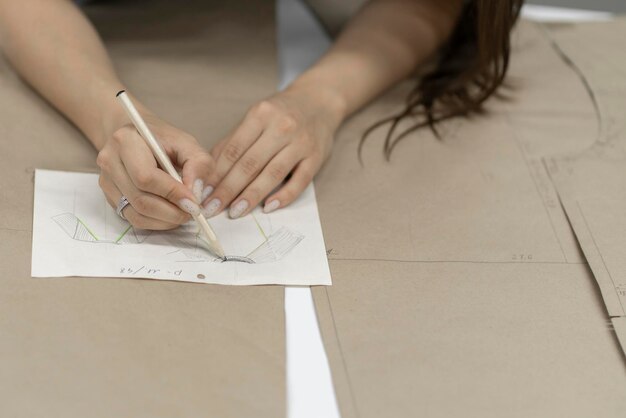 uma mão de mulher escrevendo notas no pedaço de papel em uma fábrica de costura fazendo padrões de roupas