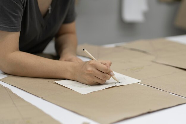 uma mão de mulher escrevendo notas no pedaço de papel em uma fábrica de costura fazendo padrões de roupas