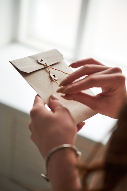 Uma mão de mulher feminina segurar abrir um envelope e cartão postal na mesa de madeira, vista superior