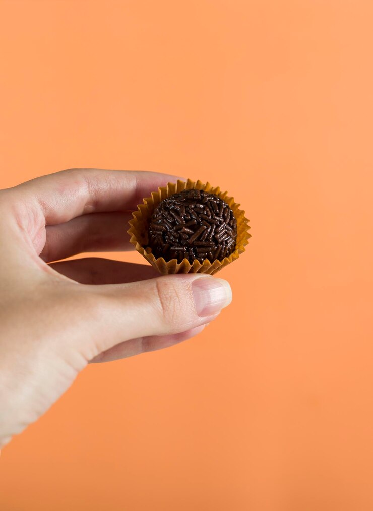 Foto uma mão de mulher segurando um brigadeiro vegano típico brasileiro doce fundo laranja