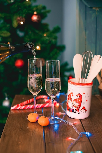 Uma mão derrama champanhe de uma garrafa em copos no fundo de uma árvore de Natal