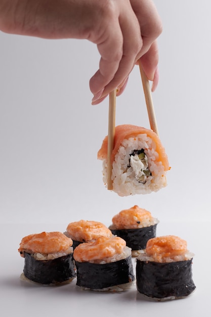 Uma mão e pauzinhos chineses segura um rolo sobre outro sushi, uma porção de comida asiática, rolos