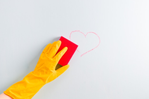 Uma mão em uma luva de borracha amarela limpa um coração marcado com giz na parede com uma esponja