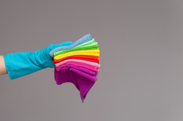 Uma mão em uma luva de borracha segura um conjunto de panos coloridos de microfibra sobre uma superfície neutra.