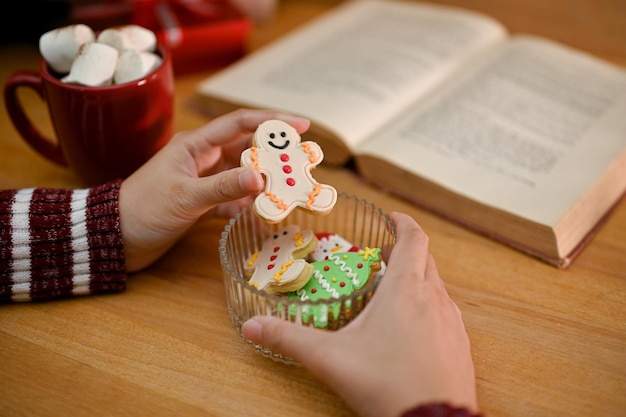 Uma mão feminina segurando um pão de gengibre fofo comendo pão de gengibre em sua mesa Conceito de Natal