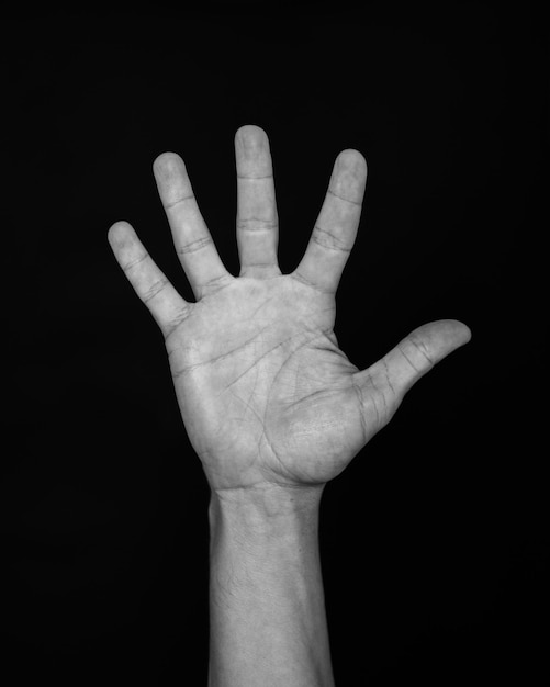 Foto uma mão humana levantada com os dedos estendidos contra um fundo preto