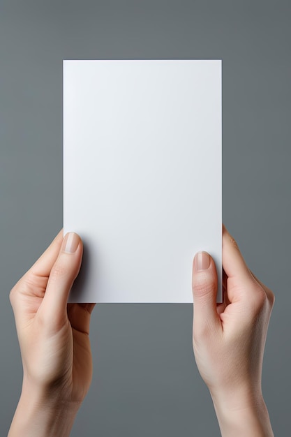 Uma mão humana segurando uma folha em branco de papel branco ou cartão isolado em fundo cinza