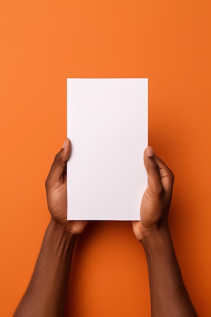 Uma mão humana segurando uma folha em branco de papel branco ou cartão isolado em fundo laranja