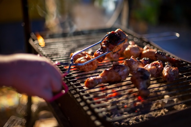 Uma mão humana vira coxinhas de frango em uma churrasqueira com pinças para grelhar. cozinhar comida em fogo aberto à noite. festa de quintal