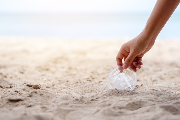 Uma mão limpando e recolhendo um lixo de vidro plástico na praia