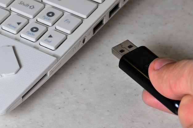 Uma mão masculina insere um cartão USB preto compacto na entrada correspondente no lado do netbook branco.