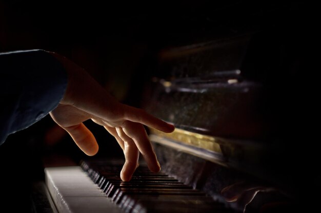 Foto uma mão masculina no piano a palma da mão está sobre as teclas e toca o instrumento de teclado na escola de música aluno aprende a tocar mãos pianista preto fundo escuro