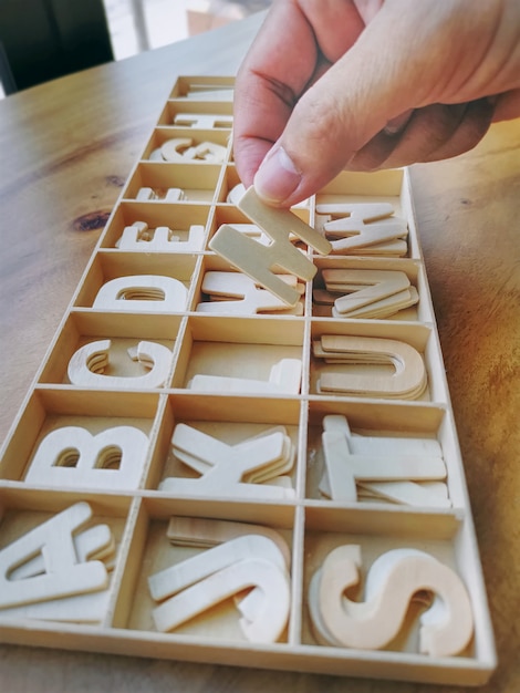 Uma mão pegando um pedaço de madeira alfabeto da bandeja