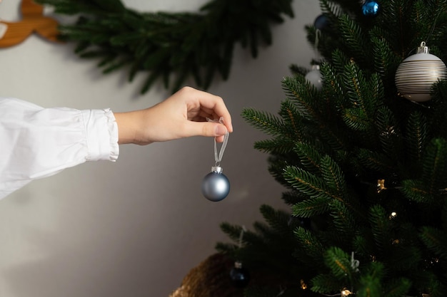 Uma mão pendura um brinquedo de bola em uma árvore de Natal artificial