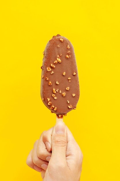 Foto uma mão segura um sorvete com nozes e cobertura de chocolate em um fundo amarelo foto vertical