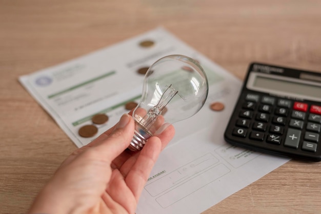 Foto uma mão segurando a lâmpada sobre a conta de eletricidade várias moedas e uma calculadora na conta conceito de preços de eletricidade e pagamento de impostos