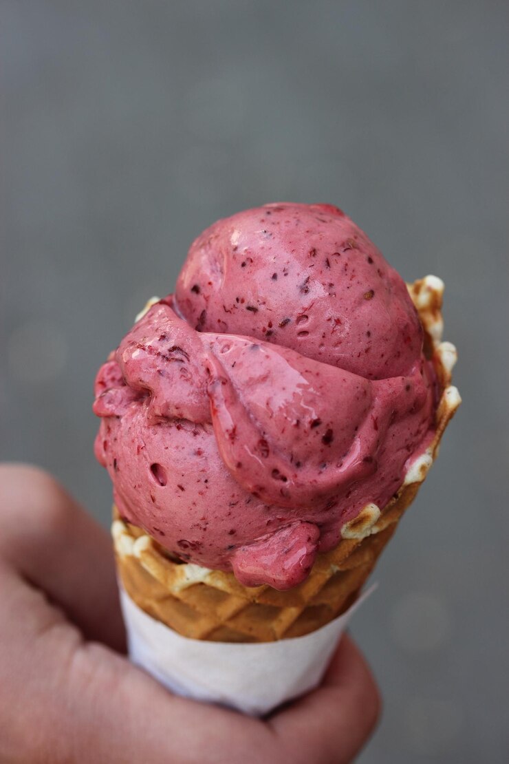 Foto uma mão segurando um cone de waffle com cobertura de frutas vermelhas.