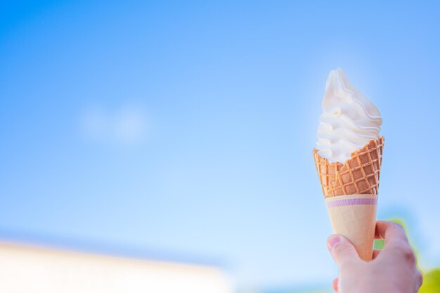 Uma mão segurando um cone de waffle com um céu azul ao fundo