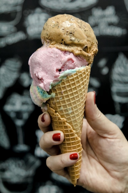 Uma mão segurando um cone de waffle com um sorvete rosa e azul