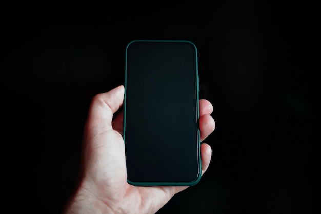 Uma mão segurando um telefone com fundo preto e a tela é um fundo preto em branco