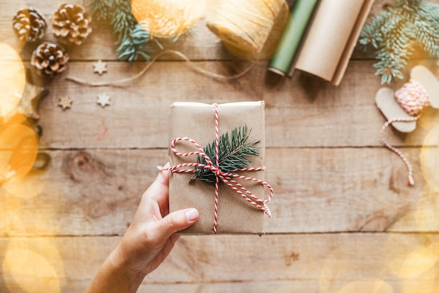 Uma mão segurando uma caixa de presente de Natal embrulhada em papel kfaft com galho de pinheiro