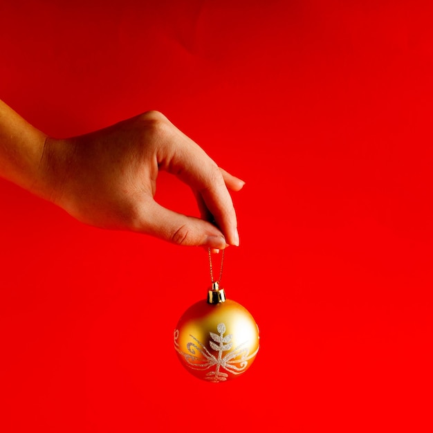 Uma mão segurando uma decoração de natal brilhante e dourada sobre fundo vermelho