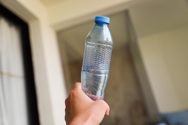 Uma mão segurando uma garrafa de água com uma tampa azul.