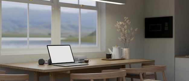 Uma maquete de laptop em uma mesa de jantar de madeira perto da janela em uma cozinha branca mínima