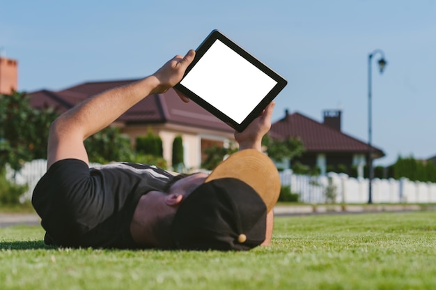 Uma maquete de um tablet nas mãos de um cara deitado no gramado.